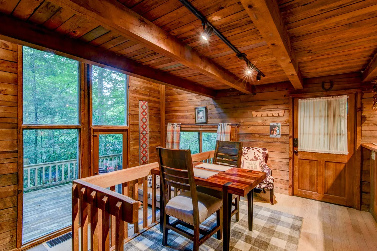 A dining space featuring a solid wooden table, large windows with nature views, wooden beams, and a decorative chair. The atmosphere is welcoming and suggests memorable shared meals, games, and quality time surrounded by the forest’s beauty.