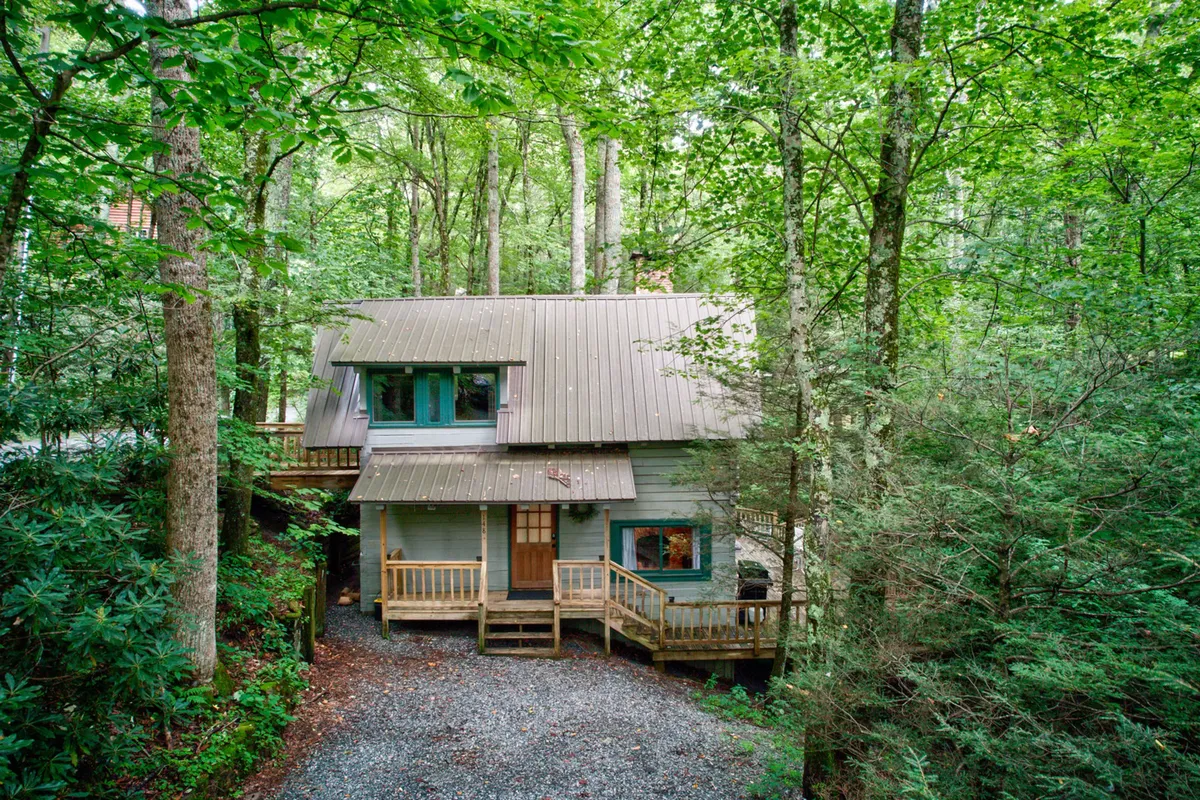 A wide shot of the cabin’s wooden deck nestled among mature trees, with large windows and a slanted roof. The deck is enveloped by the surrounding forest, creating a serene space to relax and unwind after outdoor adventures.