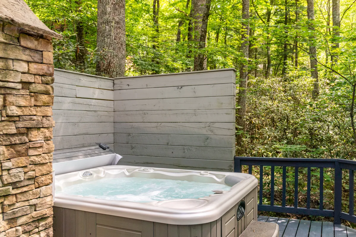 A close-up view of the hot tub nestled on the wooden deck, surrounded by lush greenery. The inviting spa promises relaxation while offering unobstructed views of the surrounding forest and sky.