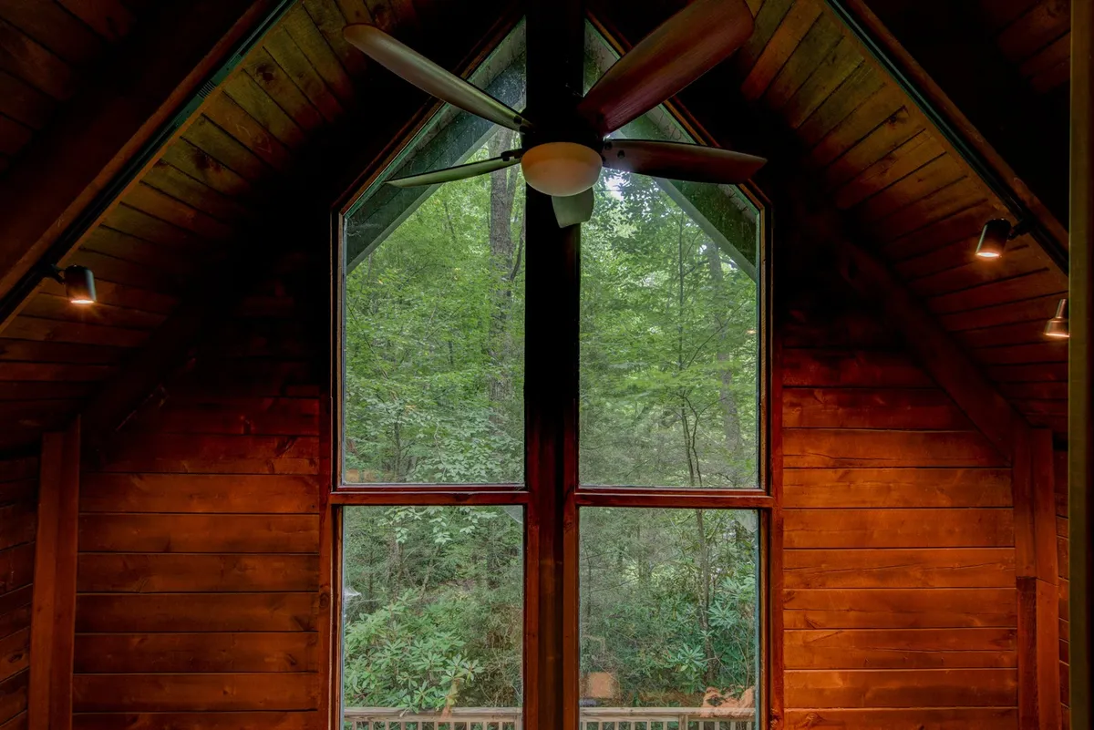A bright and peaceful living area with large windows offering sweeping views of the surrounding forest. The wooden ceiling and natural finishes create a cozy mountain cabin feel, with plenty of natural light streaming in. Through the windows, guests can watch wildlife and experience the changing seasons from the comfort of the indoors.
