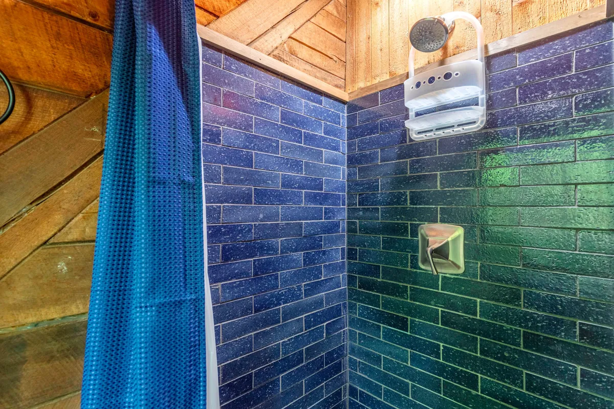 A spa-inspired bathroom with navy blue tiled walls and a modern shower head. A textured curtain and subtle lighting lend the space a calming, rejuvenating vibe, inviting relaxation after a day of adventure.